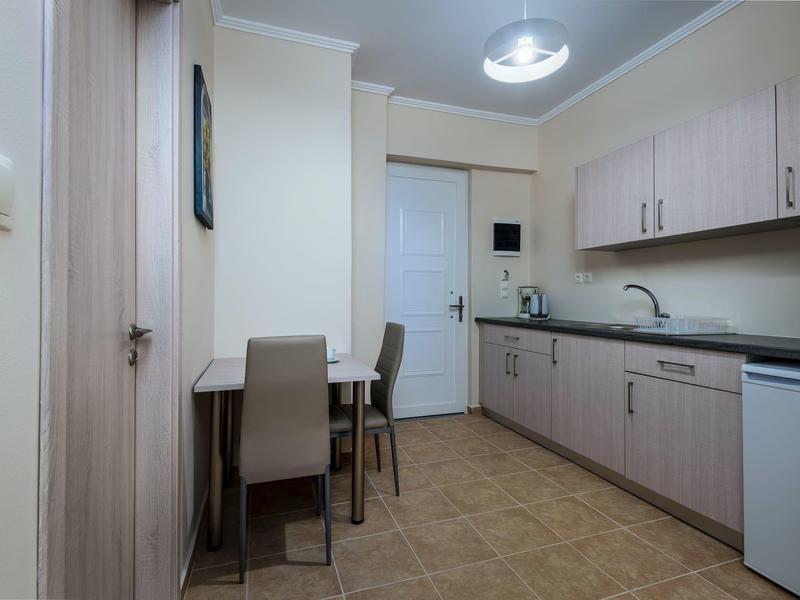 Helle Küche mit langen Holzschränken, schwarzer Arbeitsfläche, kleinem Esstisch und grauen Stühlen.