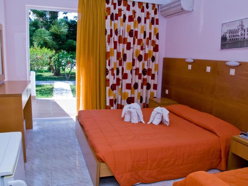 Kleines Hotelzimmer mit zwei Betten, orangener Bettwäsche und Blick in einen Garten durch offene Tür.