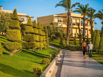 Passeggiatori su un sentiero tra giardini curati con palma e edifici dell'hotel alla luce del sole.