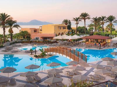 Resort con grande piscina, palme e ombrelloni al tramonto vicino al mare
