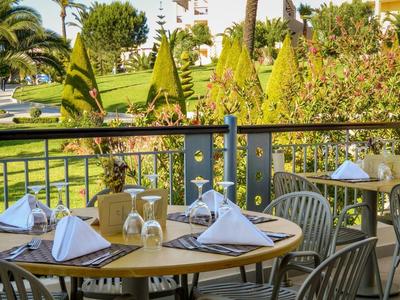 Terrazza con tavoli apparecchiati che si affacciano su un giardino tropicale al sole.
