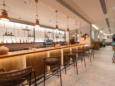 Bar d'hotel moderno con pannellature in legno, sgabelli e illuminazione calda sotto lampade a sospensione.