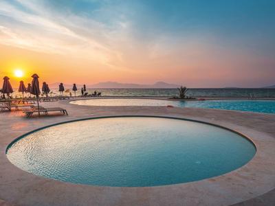 Piscina rotonda con vista sul mare al tramonto e lettini con ombrelloni.