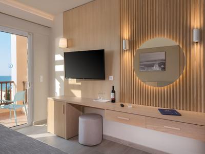 Area camera d'albergo moderna con TV, specchio, scrivania e balcone vista mare.