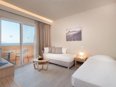 Camera d'hotel moderna con due letti singoli, piccolo tavolo e balcone con vista mare.