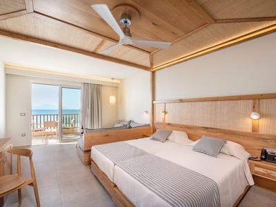 Camera d'hotel luminosa con letto matrimoniale, soffitto in legno e balcone con vista mare.