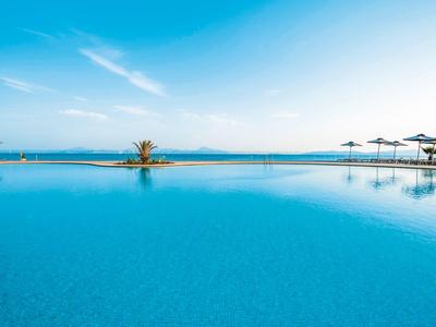 Großer Infinity-Pool mit Sonnenschirmen vor einem klaren blauen Himmel und Meerblick.