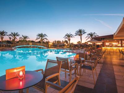 Abendliche Poollandschaft mit Tischen, Stühlen und Kerzenbeleuchtung in einem Resort.