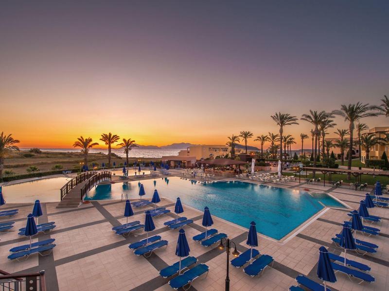 Area piscina dell'hotel con sdraio e palme al tramonto.