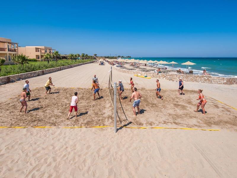 Persone che giocano a pallavolo su una spiaggia sabbiosa vicino a hotel sotto un cielo limpido.