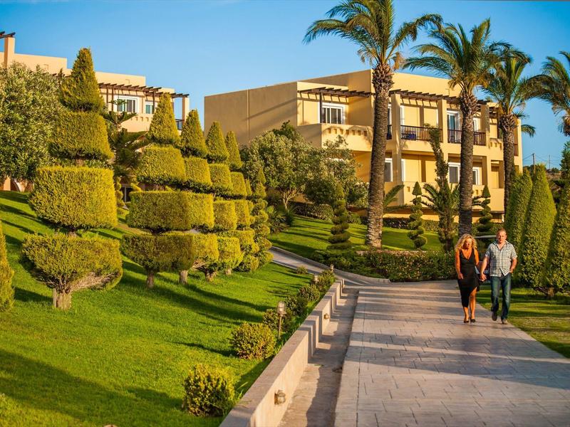 Passeggiatori su un sentiero tra giardini curati con palma e edifici dell'hotel alla luce del sole.