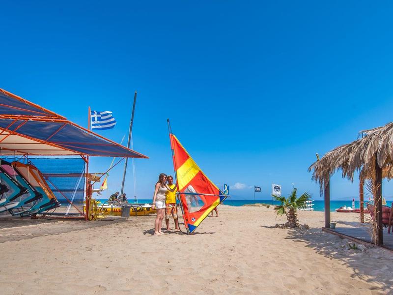 Spiaggia sabbiosa con tavole da surf, ombrelloni e vista sul mare blu sotto un cielo limpido.