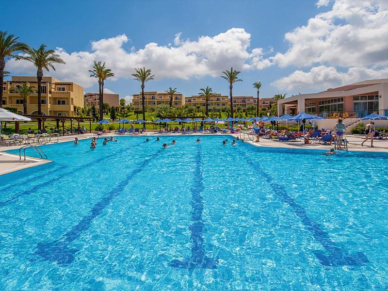 Grande piscina esterna con lettini e palme sotto un cielo azzurro in un resort.