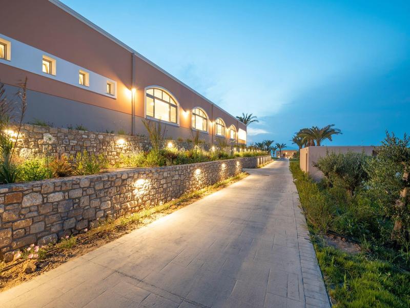 Percorso illuminato lungo un hotel con muro di pietra e piante al crepuscolo.