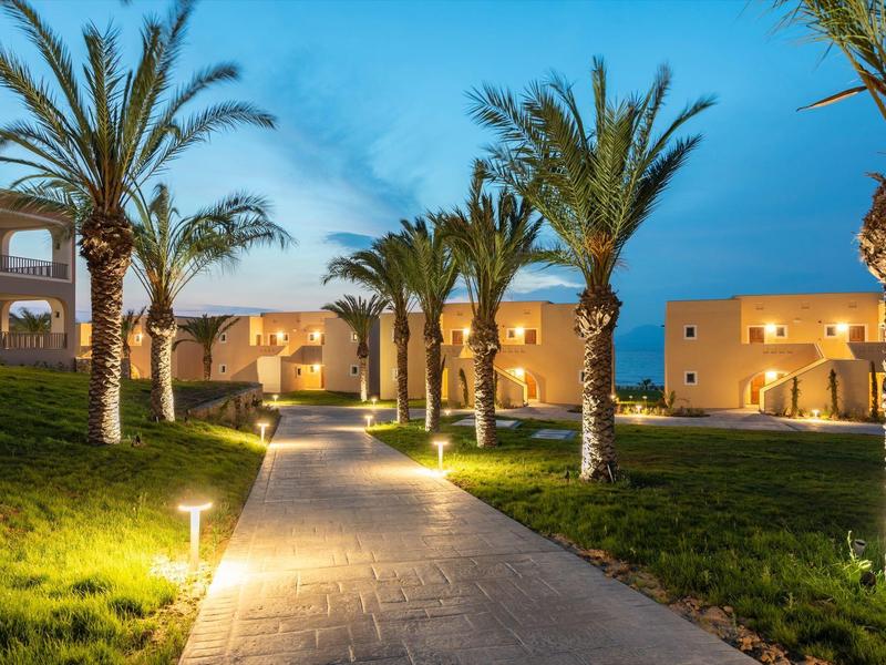 Sentiero illuminato fiancheggiato da palme che conduce a un edificio dell'hotel al crepuscolo.