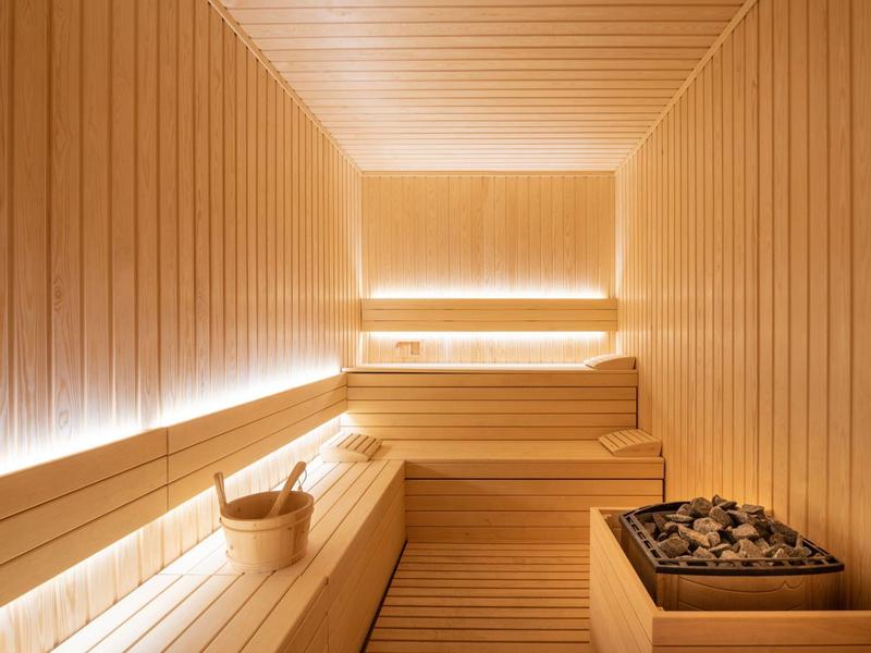 Sauna finlandese luminosa con panche in legno, una stufa per sauna e un secchio con mestolo.