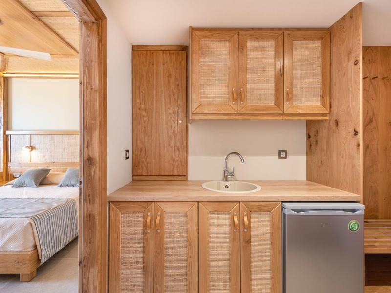 Piccola angolo cottura con mobili in legno, lavandino e mini frigorifero accanto a una camera da letto.