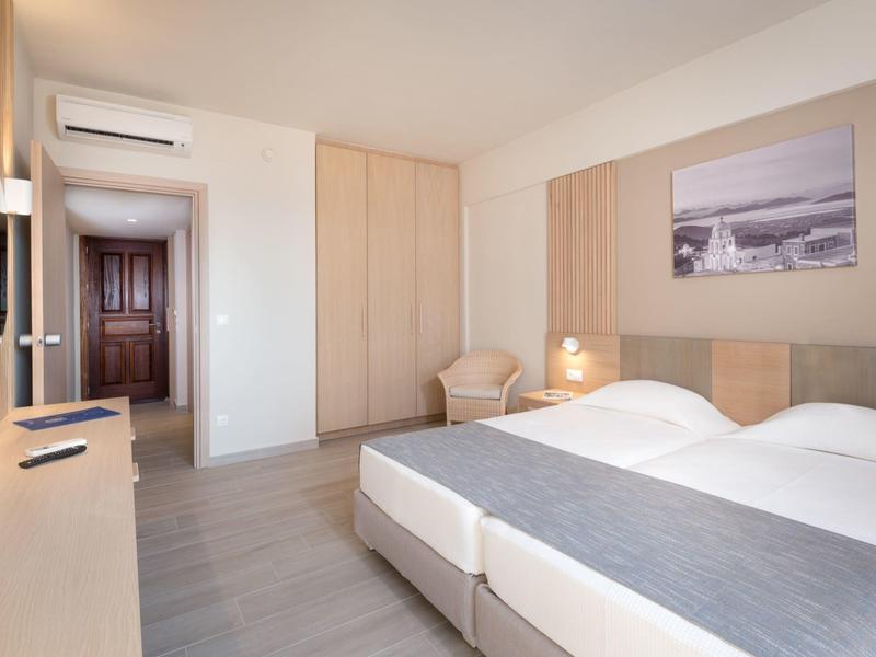 Camera d'albergo luminosa con due letti singoli, armadio, poltrona e arredamento moderno.