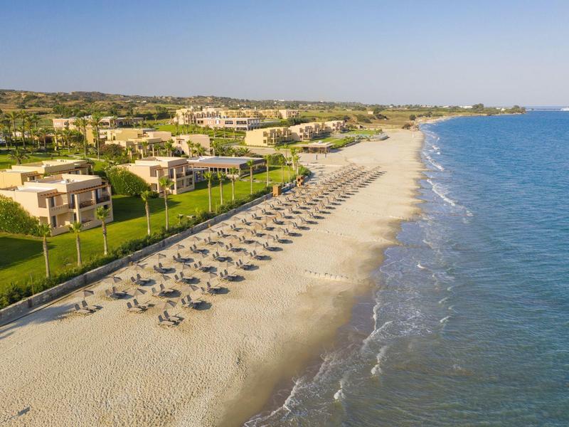 Spiaggia di sabbia vuota con file di lettini vicino a un'area alberghiera sul mare.