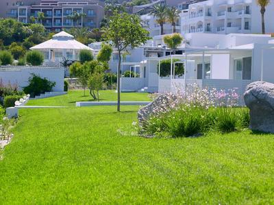 Giardino verde con alberi e fiori davanti a edifici bianchi dell'hotel in una giornata di sole.