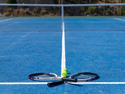 Two tennis rackets and a ball lie at the center of a blue tennis court near the net.