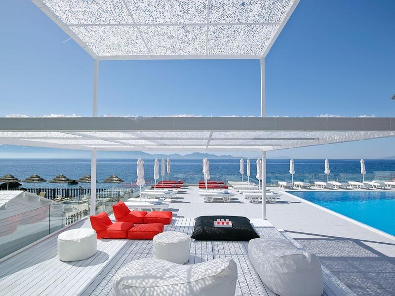 Area piscina moderna con mobili lounge rossi e vista sul mare sotto un cielo sereno.