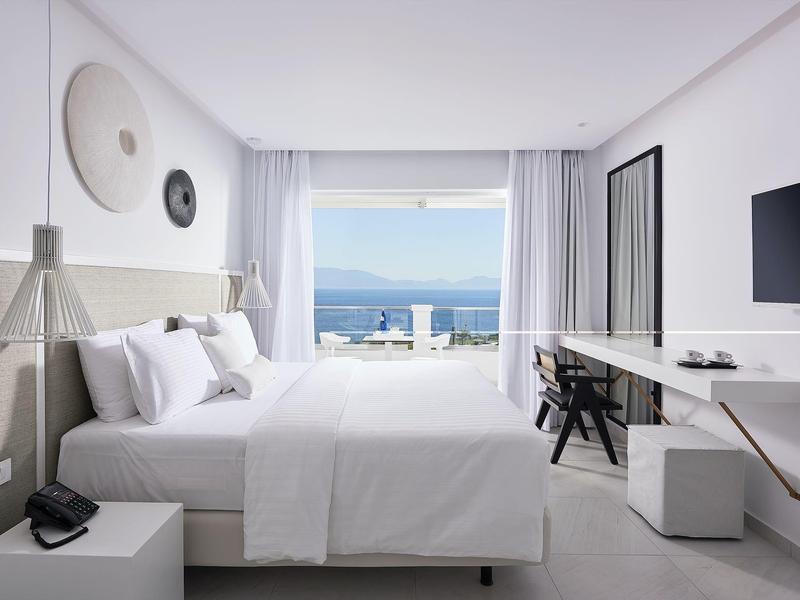 Camera d'hotel moderna con letto matrimoniale, scrivania e vista mare attraverso grandi finestre