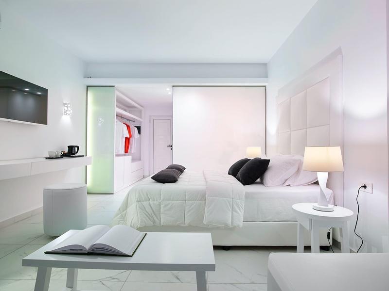 Camera d'hotel moderna con letto grande, arredi bianchi e porta aperta verso il guardaroba.