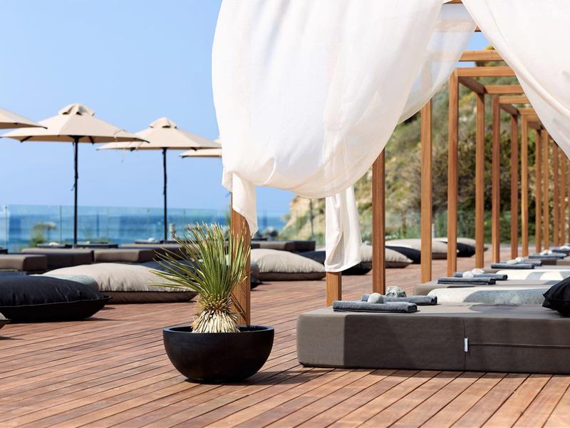 Lussuosa terrazza sul tetto con lettini, tende bianche e vista sul mare sotto un cielo azzurro.
