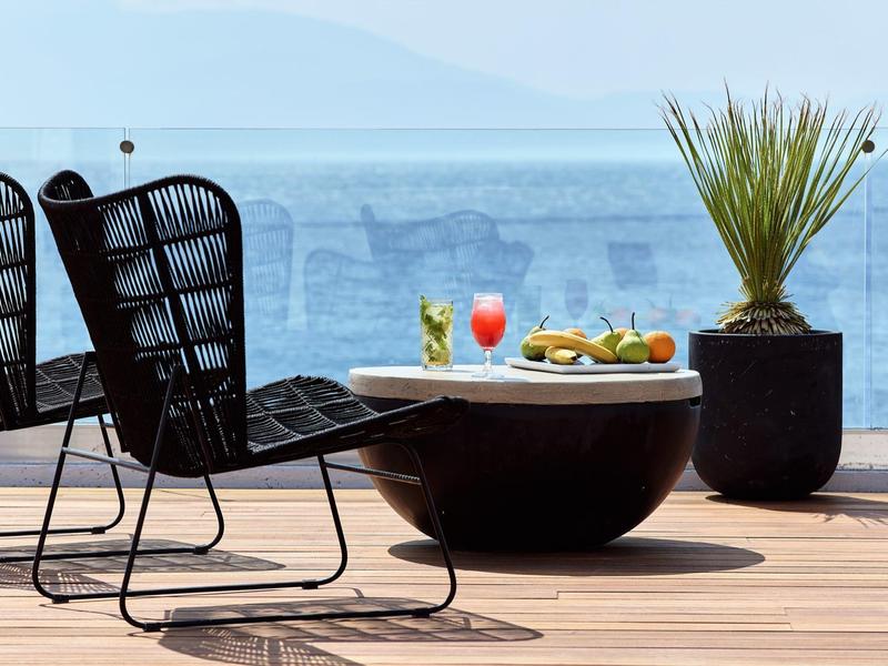 Terrazza con sedie moderne, tavolo con bevande e snack, vista sul mare.