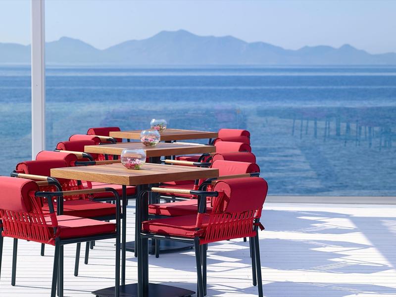 Area terrazza con sedie rosse e tavoli in legno con vista sul mare e sulle montagne.