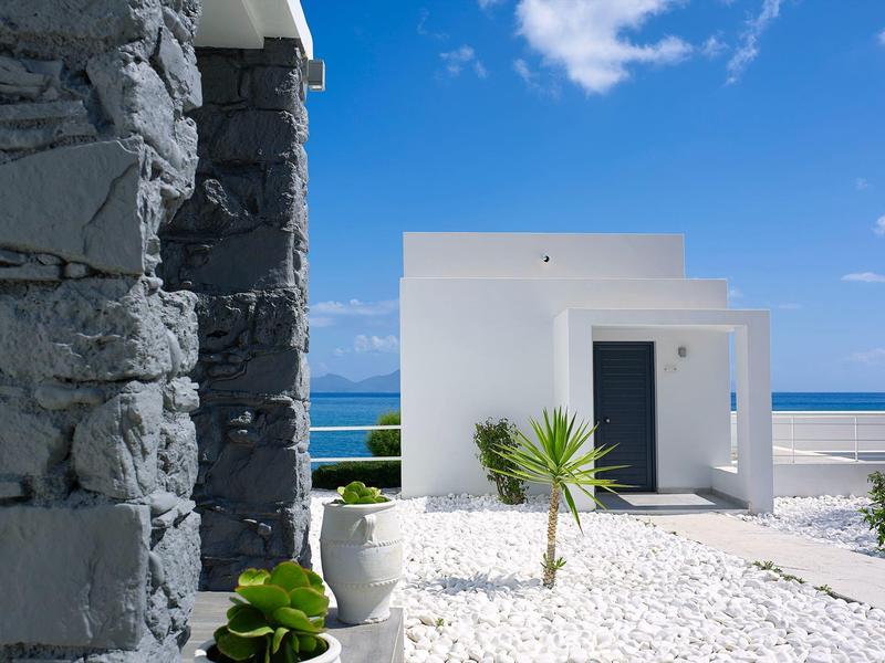 Edificio bianco moderno sulla spiaggia con pavimento in ciottoli e vista mare.