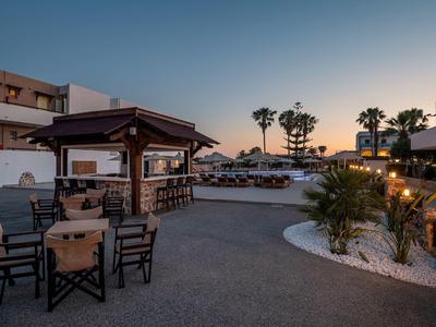 Terrazza dell'hotel con tavoli e sedie, piccolo padiglione e giardino di palme al tramonto.