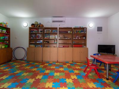 Sala giochi per bambini con pavimento a puzzle colorato, mobili in legno, TV e tavolo da gioco.
