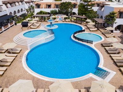 Piscina d'hotel con acqua blu circondata da lettini e edifici bianchi.