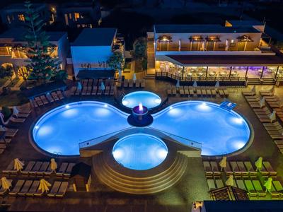 Piscina illuminata con tre vasche rotonde accanto a un edificio alberghiero di notte.