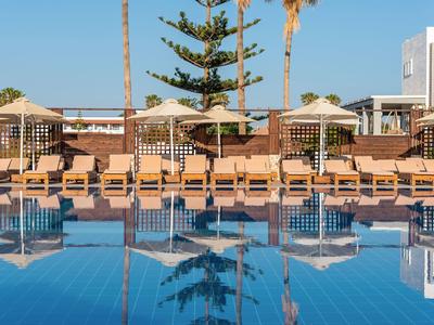 Area piscina con lettini e ombrelloni davanti agli edifici dell'hotel in una giornata di sole