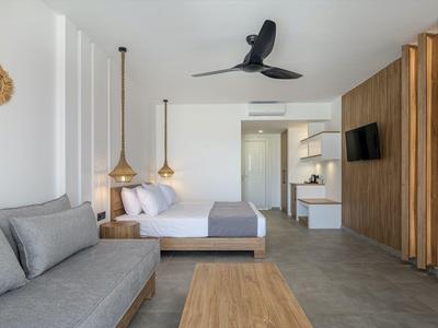 Camera d'hotel moderna con letto matrimoniale, divano, ventilatore a soffitto e dettagli in legno sulla parete.