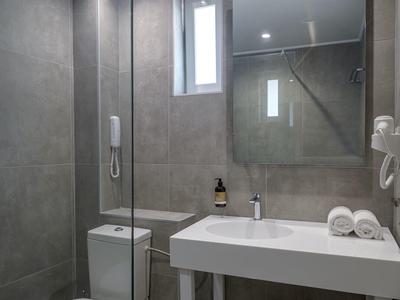 Bagno moderno con piastrelle grigie, lavabo bianco, WC e asciugamani sotto il lavabo.