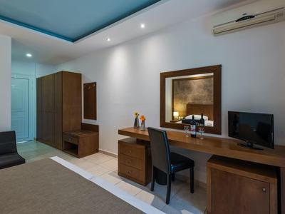 Camera d'hotel moderna con scrivania, sedia, TV e armadio in tonalità neutre.