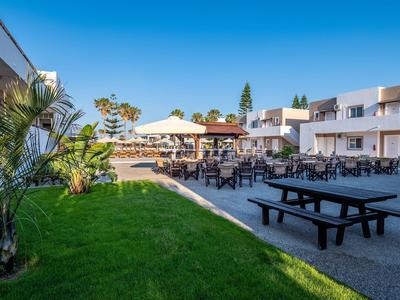Area esterna di un hotel con giardino, posti a sedere e ombrelloni sotto un cielo azzurro.