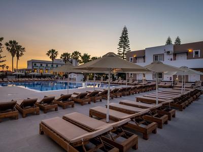 Lettini vuoti accanto a una piscina con ombrelloni al tramonto in un hotel.