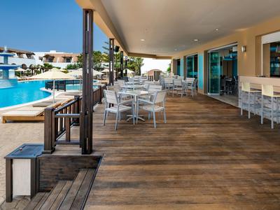 Terrazza coperta con tavoli e sedie accanto alla piscina e al bar dell'hotel alla luce del sole.