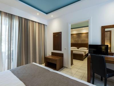 Camera d'hotel moderna con tende, letto, scrivania e camera adiacente con letto matrimoniale.