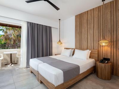 Camera d'hotel moderna con letto matrimoniale, parete in legno e balcone con tavolo e sedie.