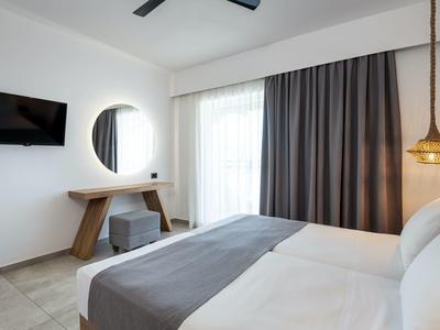 Camera d'hotel moderna con letto, TV, specchio, finestra con tende e lampada sospesa.