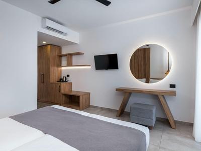 Camera d'albergo moderna con letto grigio, specchio circolare illuminato e TV a parete.