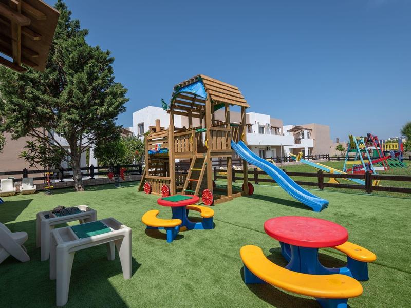 Area giochi per bambini con scivolo, tavoli e sedie colorati davanti a case vacanze moderne.