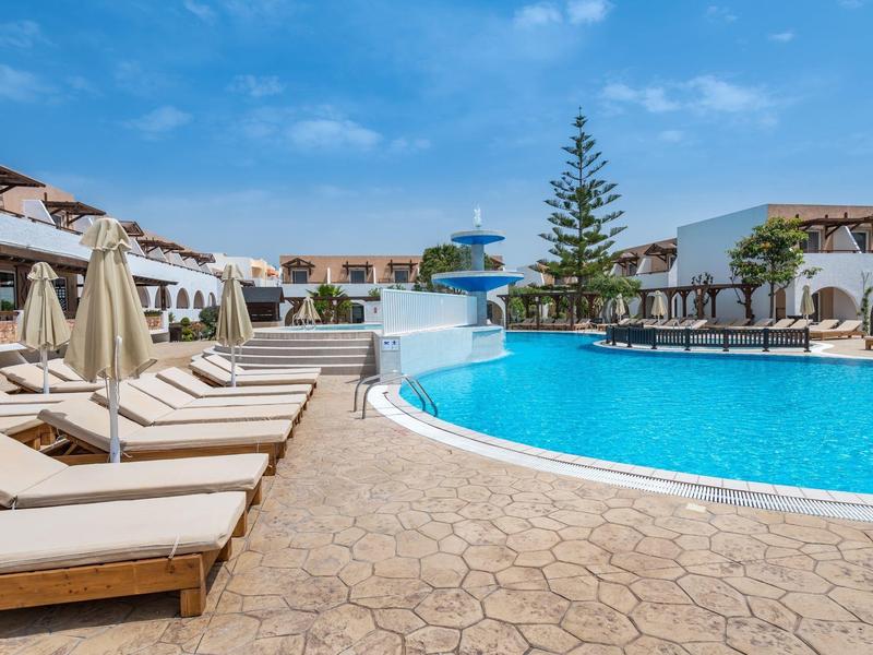 Grande piscina dell'hotel con lettini e ombrelloni sotto un cielo blu.