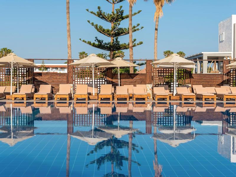 Area piscina con lettini e ombrelloni davanti agli edifici dell'hotel in una giornata di sole